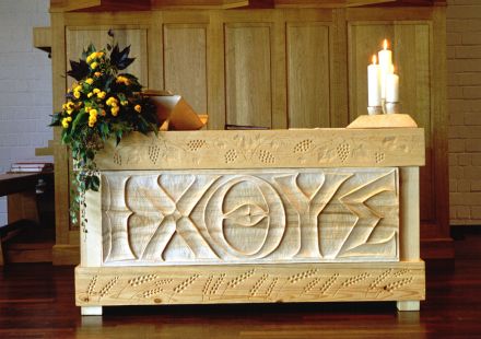 Ein Bild des Altars. Links bedeckt von Blumenschmuck, der eine aufgeschlagene Bibel leicht verdeckt. Rechts drei Kerzen. Im Hintergrund ein Teil derOrgel.