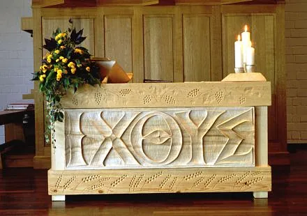 Ein Bild des Altars. Links bedeckt von Blumenschmuck, der eine aufgeschlagene Bibel leicht verdeckt. Rechts drei Kerzen. Im Hintergrund ein Teil derOrgel.