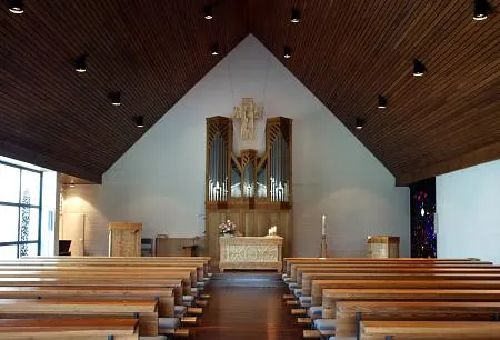 Bild der Erlöserkirche von innen. Im Vordergrund sind die alten Kirchbänke zu sehen. Im Hintergrund sind in der Mitte Altar Orgel und Kreuz zu sehen. Rechts hinten das Taufbecken und links hinten die Kanzel.