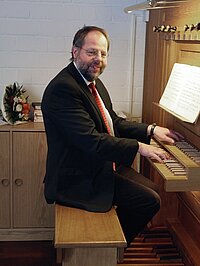 Thomas Schulze-Athens sitzt in Anzug und Krawatte an der Orgel und schaut freundlich zum Betrachter.