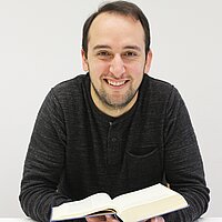 Pfarrer Felix Klemme lächelt den Betrachter an. In der linken Hand hält er eine aufgeschlagene Bibel.